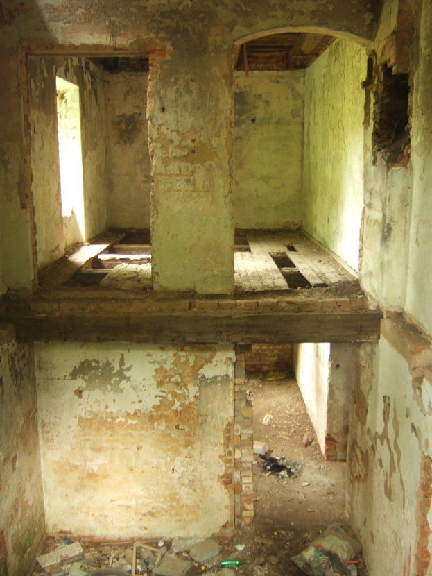 Ein alter Raum mit abblättender Farbe, einem zentralen Fenster und verstreuten Gegenständen auf dem Boden, ähnlich einem Luftschutzbunker.