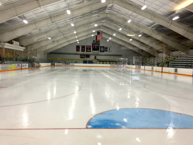 Großes Hallen-Eisstadion mit Deckenbeleuchtung, Werbetafeln, einer Rückwand, Treppen mit Geländern und einigen Menschen, wahrscheinlich eine Hockey-Anlage.
