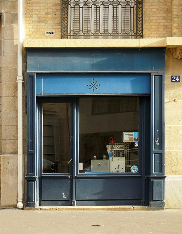 Gebäude mit blauer Tür und Fenstern, ein Rohr an der Wand, ein Geländer oben und eine Straße unten.