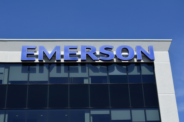 Das Emerson-Logo und der Text "Emerson investiert 1,5 Milliarden US-Dollar in den USA" an der Seite eines Gebäudes vor einem klaren blauen Himmel.