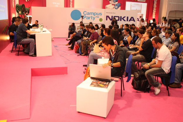 Eine Konferenzszene mit Sitzplätzen und einer Bühne, auf der eine Diskussion zwischen Medienvertretern und -eigentümern stattfindet, mit einem großen Banner und einer Wand im Hintergrund.