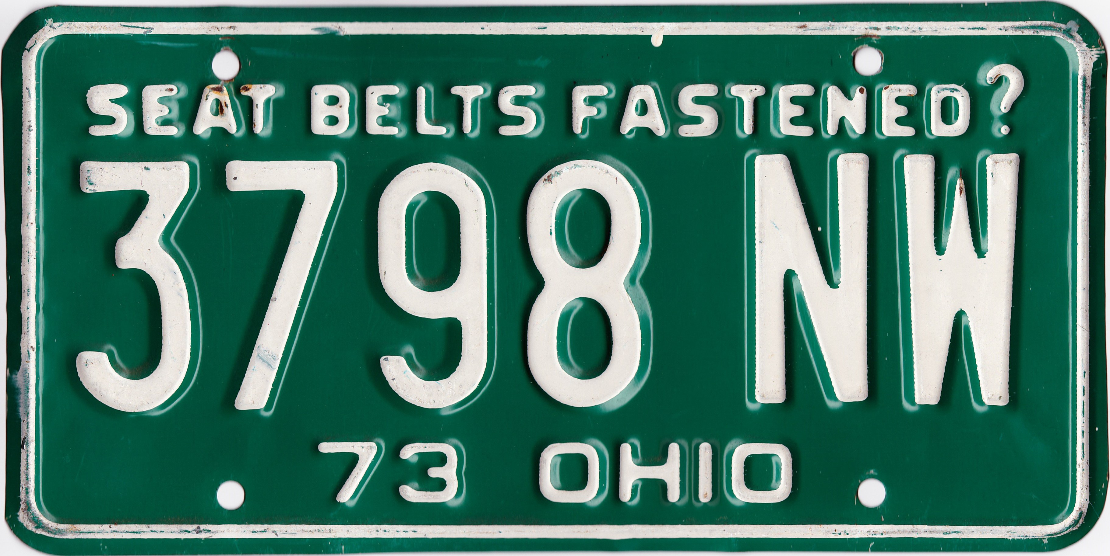 Grünes Ohio-Kennzeichen mit weißer Schrift, die 'Seat Belts Fastened?' auf einem weißen Hintergrund liest.