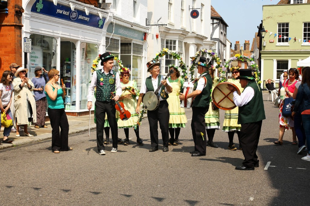 Eine Gruppe von Musikern, die Instrumente auf der Straße spielen, mit einer kleinen Menge drum herum und Geschäften mit Schildern im Hintergrund.