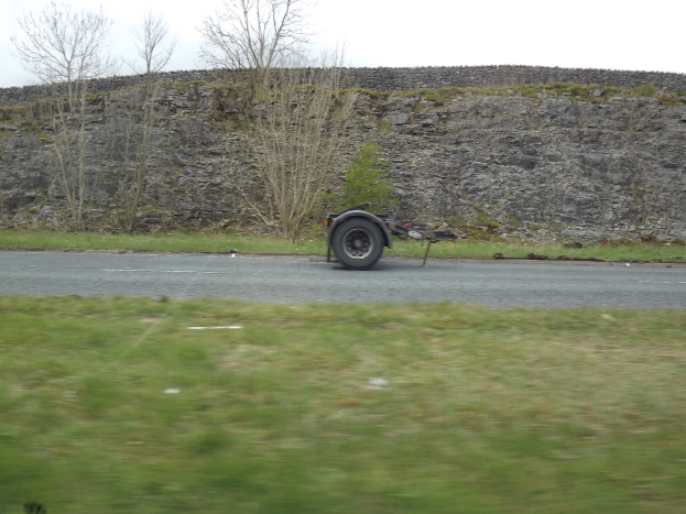 Ein Lkw-Rad auf einer Straße mit Gras, Bäumen und Felsen auf beiden Seiten.