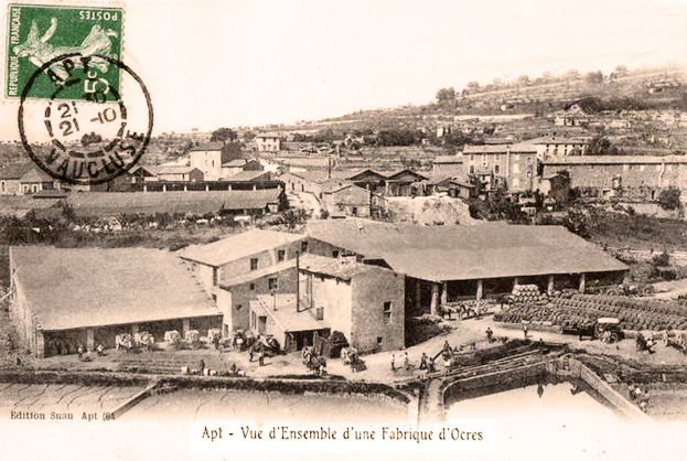 Ein altes Schwarz-Wei├č-Foto einer Stadt mit einem Stempel, das Geb├Ąude, B├Ąume und Menschen zeigt, mit Text unten.