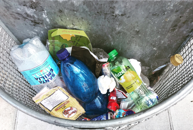 Ein Metallmüllcontainer voller Plastikflaschen, Tüten und anderen Gegenständen.