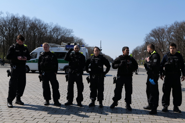 Eine Gruppe von Polizisten vor einem Krankenwagen auf einer Straße mit Bäumen, Laternen und einem klaren Himmel.