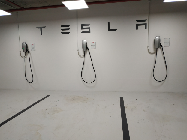 Eine Tesla-Ladestation in einer Tiefgarage mit angebrachten Ladekabeln und Deckenbeleuchtung, die die darunterliegende Etage zeigt.