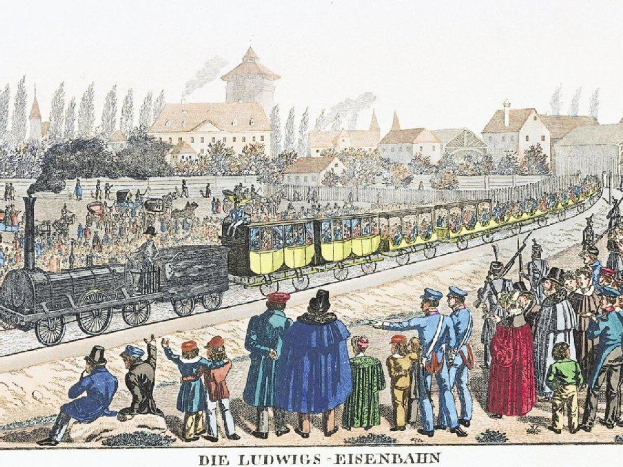 Gruppe von Menschen um einen Zug auf Schienen mit einigen Fahrgästen im Zug und anderen außerhalb, mit Gebäuden und Bäumen im Hintergrund und dem Text "Ludwigs-Eisenbahn, die erste Bahnstation in Deutschland" unten.