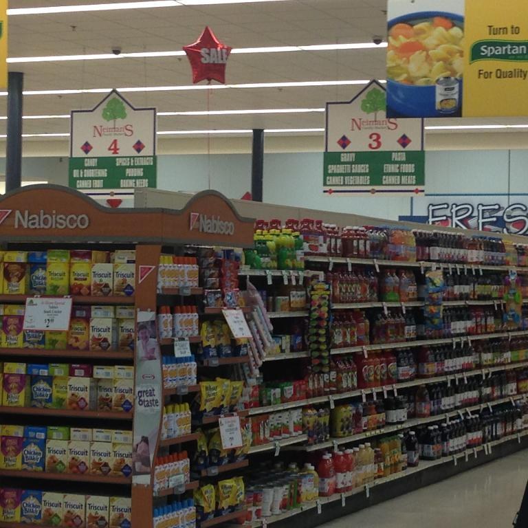 Ein Supermarkt-Innenraum mit an der Decke angebrachten Leuchten und Schildern, auf denen Lebensmittel auf Regalen zu sehen sind.