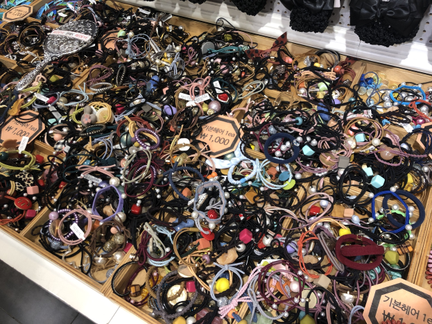 Vitrine mit verschiedenen Schmuckstücken einschließlich Armbändern, Ketten und Preisschildern, mit Kleidung darüber, wahrscheinlich auf einem Markt.