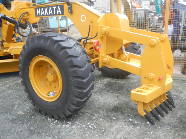 Gelber Radlader mit gelbem Schutzhelm auf einem Parkplatz vor einem Gebäude mit Metallzaun und blauem Himmel im Hintergrund.