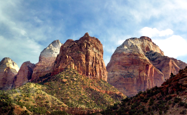 Zion-Nationalpark in Utah mit majestätischen Bergen, grünen Bäumen, felsigem Gelände und einem Himmel voller weißer Wolken.