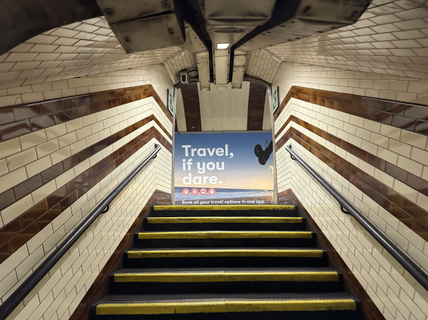 Eine Treppe in einer U-Bahn-Station mit einem 'Reise, wenn du wagst' Schild oben, flankiert von Geländern und sichtbaren Stationwänden.
