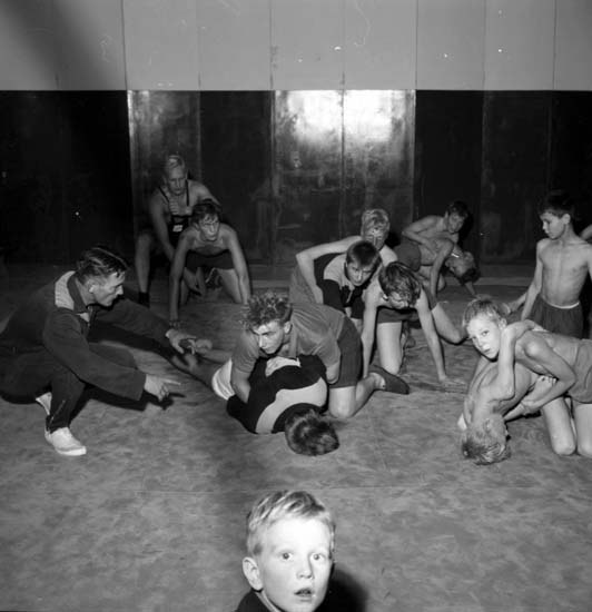 Schwarz-weißes Bild von jungen Jungs, die in einem Gym ringen, mit einer Wand im Hintergrund.