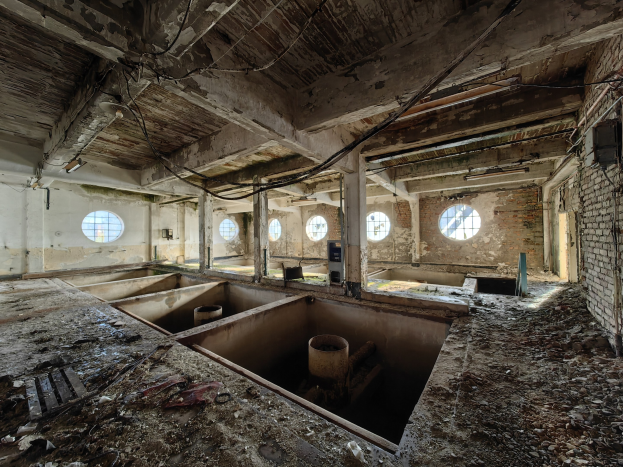 Abandonierter Gebäudeinnenraum im Sperrgebiet von Tschernobyl mit verstreuten Trümmern, freiliegenden Wänden, Decke und mehreren Fenstern und Säulen.