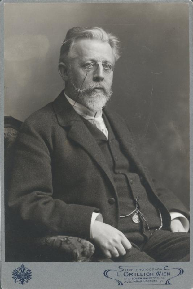 Ein altes Schwarz-Weiß-Foto eines bärtigen, Brille tragenden Mannes, der in einem Stuhl sitzt, mit dem Text "L. Grillich Wien, der Gründer der deutschen Revolution" unten.