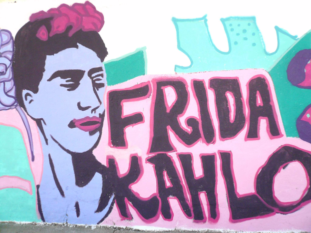 Ein leuchtendes Frida-Kahlo-Mosaik auf einem Gebäude in Mexiko-Stadt, das ihr Porträt mit einer Blume im Haar und den Text 'Fridakahlo' in fetten, schwarzen Buchstaben zeigt.