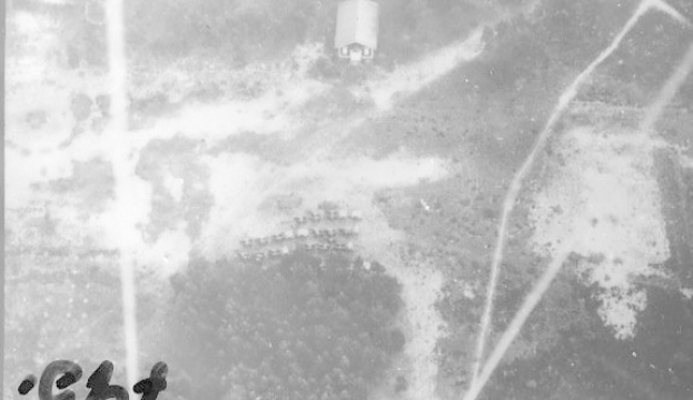 Schwarz-weißes Foto eines Flugzeugs, das über ein Feld mit einem Gebäude im Hintergrund fliegt, mit der Beschriftung "Weltkrieg II US Air Force" unten.