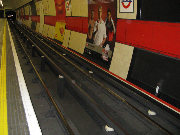 Eine Bahnschiene mit Plakaten an der Wand daneben.