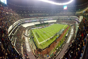 Ein großes Stadion voller Zuschauer, die ein Fußballspiel verfolgen, mit Spielern und verschiedenen Objekten auf dem Feld, beleuchteten Tafeln, Geländern, Bildschirmen und Deckenleuchten.