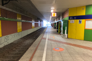 Ein Bahnhofsgebäude in Berlin, Deutschland, mit einem Zug auf den Schienen, beleuchtet von Deckenlampen, Graffiti an der linken Wand und einigen Gegenständen auf der rechten Seite.