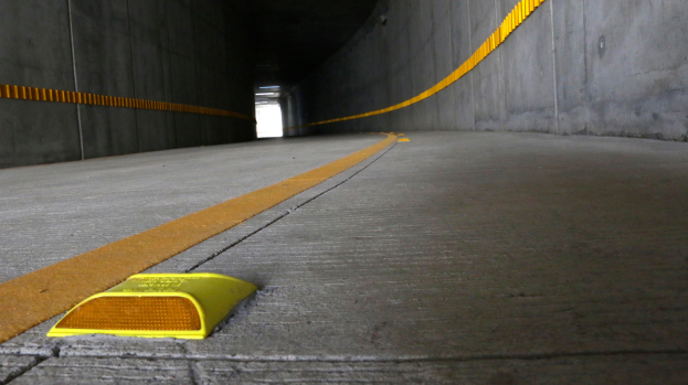 Ein Tunnel mit Wänden auf beiden Seiten und gelbem Absperrband auf dem Boden, mit einer Lampe im Hintergrund.