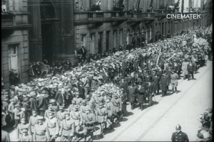 Schwarzes Foto einer Parade mit einer großen Menge, die eine Straße entlangmarschiert, einige halten Gewehre, vor einem Gebäude mit einem sichtbaren Wasserzeichen.