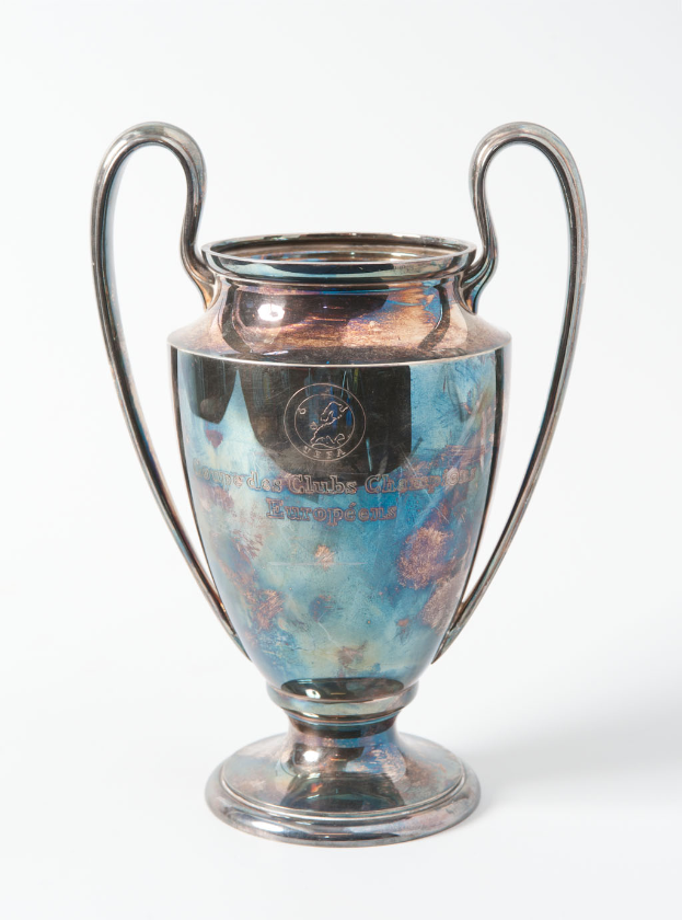 Der UEFA-Champions-League-Pokal, ein stählerner Becher mit zwei Griffen und einem blauen und silbernen Farbschema, mit der Inschrift «UEFA Champions League», vor einem weißen Hintergrund.