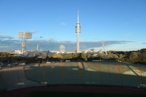 Olympiastadion in Berlin, Deutschland, mit dem Fernsehturm im Hintergrund, umgeben von Bäumen, Gebäuden und Lichtern, unter einem bewölkten Himmel.