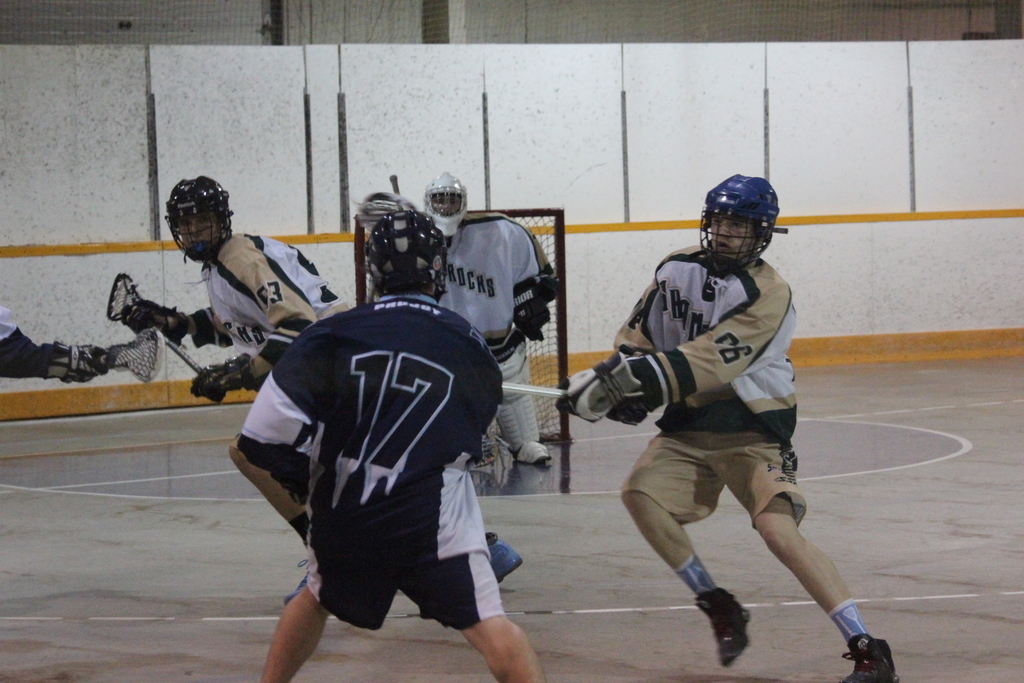 Menschen in Helmen mit Stöcken scheinen in einem Innenraum zu kämpfen, im Hintergrund ein Netz.