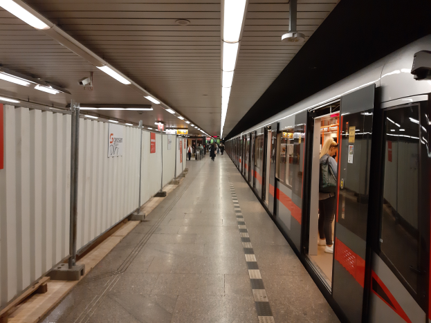 Eine U-Bahn fährt in einem Bahnhof in Berlin, Deutschland, mit Menschen auf dem Bahnsteig, Gegenständen auf dem Boden links und Lampen an der Decke.