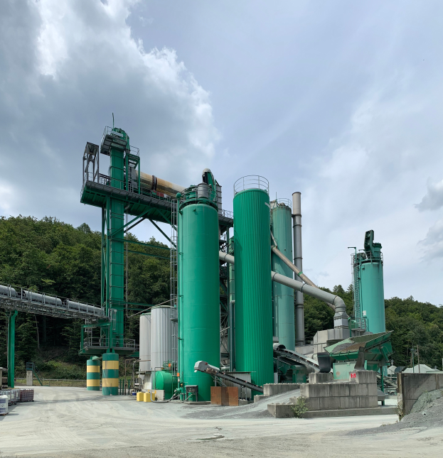 Eine große industrielle Pyrolyseanlage für Altreifen mit zahlreichen grünen Tanks, Maschinen und Polen, vor einem Hintergrund aus Bäumen und einer bewölkten Himmel.
