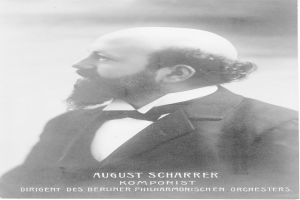 Ein Schwarz-Wei├č-Foto von August Scharrer, einem deutschen Komponisten, der einen Blazer und eine Schleife tr├Ągt, mit Text am unteren Bildrand.