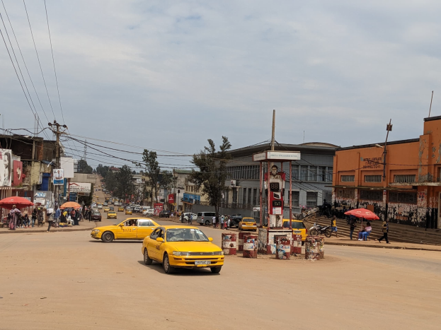 Ein gelbes Taxi fährt eine belebte Stadtstraße entlang, die von Gebäuden gesäumt ist, während Fußgänger mit Regenschirmen auf dem Gehweg gehen.