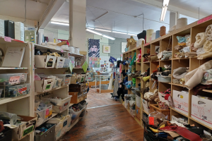 Ein chaotischer Bastelladen in New York City mit verschiedenen Artikeln auf Gestellen und einem Tisch, einer zentralen Säule und Deckenleuchten.