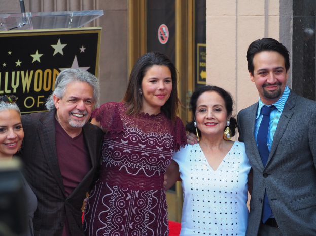 Gruppe von Menschen auf einem roten Teppich bei der Zeremonie des Hollywood Walk of Fame posend, mit einer Tafel, einem Glaspodest und einer Wand im Hintergrund.