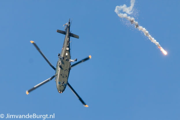 Ein militärisches Hubschrauberflugzeug, das eine Rakete hält, die Rauch und Feuer ausstößt, mit Text in der linken unteren Ecke.