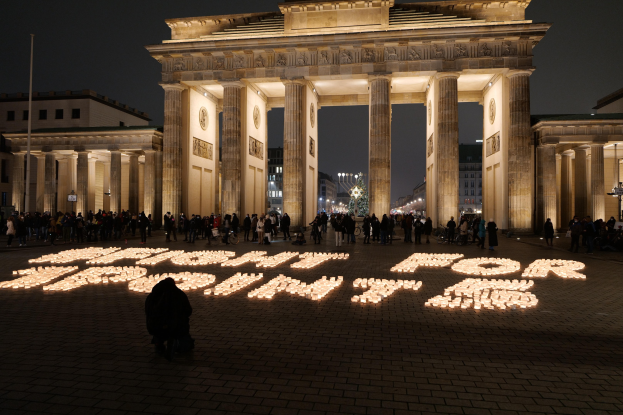 Eine Gruppe von Menschen steht vor dem beleuchteten Reichstagsgebäude in Berlin, Deutschland, mit Gebäuden, Polen und Lichtern drumherum und den Worten "Kampf für Freiheit" auf dem Boden im Vordergrund.