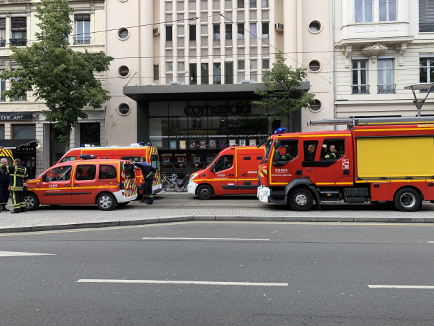 Eine Gruppe von Feuerwehrautos auf einer Straße in Paris geparkt, mit Menschen in der Nähe, vor Häusern, Bäumen und einem Fahrrad im Hintergrund.