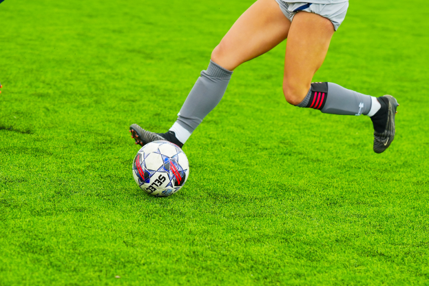 Eine Frau in Sportbekleidung und -schuhen schießt einen Fußball auf einem grünen Rasen.
