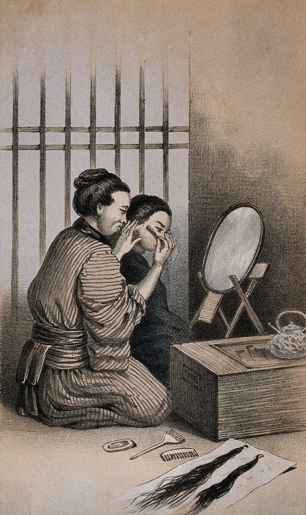 Eine Frau sitzt auf dem Boden vor einem Spiegel und schminkt sich, umgeben von einer Box, einer Bürste, einem Kamm und anderen Gegenständen auf einem Tisch, mit einer Wand und einem Fenster im Hintergrund.