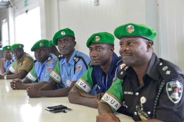 Eine Gruppe von Polizeibeamten sitzt an einem Tisch während einer Schulung, mit Mobiltelefonen und anderen Gegenständen auf dem Tisch, in einem Raum mit Fenstern und Deckenbeleuchtung.