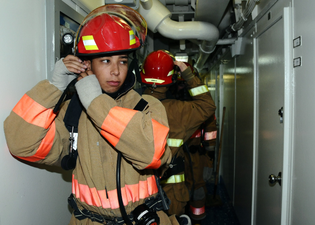 Feuerwehrleute in Uniform stehend in einem Raum mit Rohren und Geräten während einer Übung.