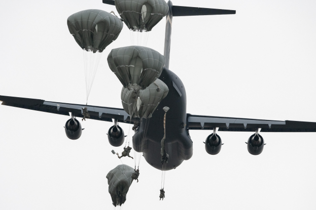 Ein großes Militärluftfahrzeug mit mehreren Fallschirmen, das gegen einen klaren blauen Himmel fliegt.