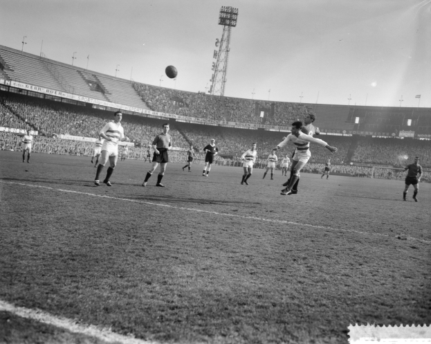 Eine Gruppe von Männern, die Fußball auf einem Feld mit Stadion, Flutlicht und klarem Himmel spielen.