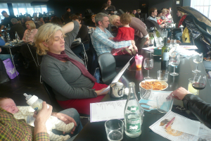 Einblicke in ein volles Restaurant mit Menschen an Tischen, die Gläser, Teller mit Essen, Getränkeflaschen, Speisekarten und andere Gegenstände haben.