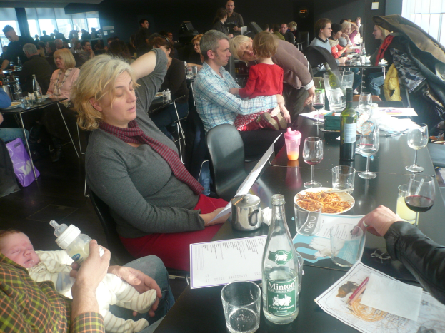 Einblicke in ein volles Restaurant mit Menschen an Tischen, die Gläser, Teller mit Essen, Getränkeflaschen, Speisekarten und andere Gegenstände haben.