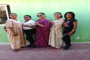 Eine Gruppe von Frauen steht zusammen vor einer grünen Wand mit einem Fenster auf der linken Seite und nimmt an einem Internationalen Frauentag-Event teil.