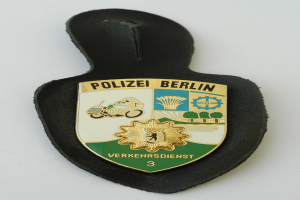 Ein schildförmiges Polizeibadgebnis mit der Aufschrift 'Polizei Berlin' auf einem blauen Hintergrund, einem weißen Rand, einem weißen zentralen Stern und schwarzer fetter Schrift auf einer Oberfläche.